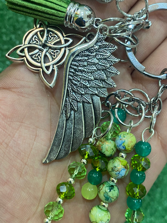 Llavero plateado con tonos verdes con pieza central de ala y nudo de bruja
